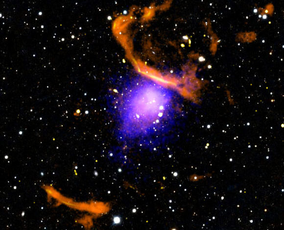 This new composite image made with X-rays from NASA’s Chandra X-ray Observatory (blue and purple), radio data from the MeerKAT radio telescope (orange and yellow), and an optical image from PanSTARRS (red, green, and blue) shows the massive galaxy cluster PLCK G287.0+32.9. Image credit: NASA / CXC / CfA / Rajpurohit et al. / PanSTARRS / SARAO / MeerKAT / SAO / N. Wolk.