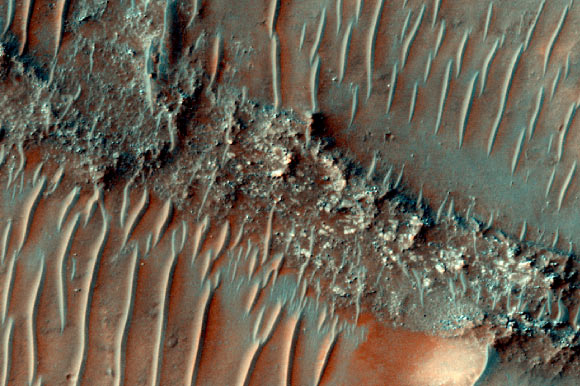 This HiRISE image shows a flat top, heavily eroded fluvial sinuous ridge on Mars; sand dunes can be seen migrating over the top of the fluvial sinuous ridge. Image credit: NASA / JPL / University of Arizona.
