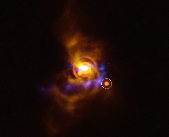 This image shows a possible substellar companion orbiting the young star V960 Mon. The candidate object was found with ESO’s Very Large Telescope (VLT), using its new Enhanced Resolution Imager and Spectrograph (ERIS). The new ERIS data are shown here in orange, overlaid on older images of the dusty disk as seen with the VLT’s SPHERE instrument (yellow) and ALMA (blue). Image credit: ESO / A. Dasgupta / ALMA / ESO / NAOJ / NRAO / Weber et al.