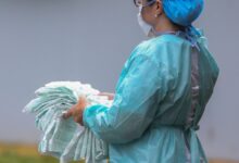 Cientista em laboratório avalia dados de vírus, com tela e microscópio, em foco concentrado.